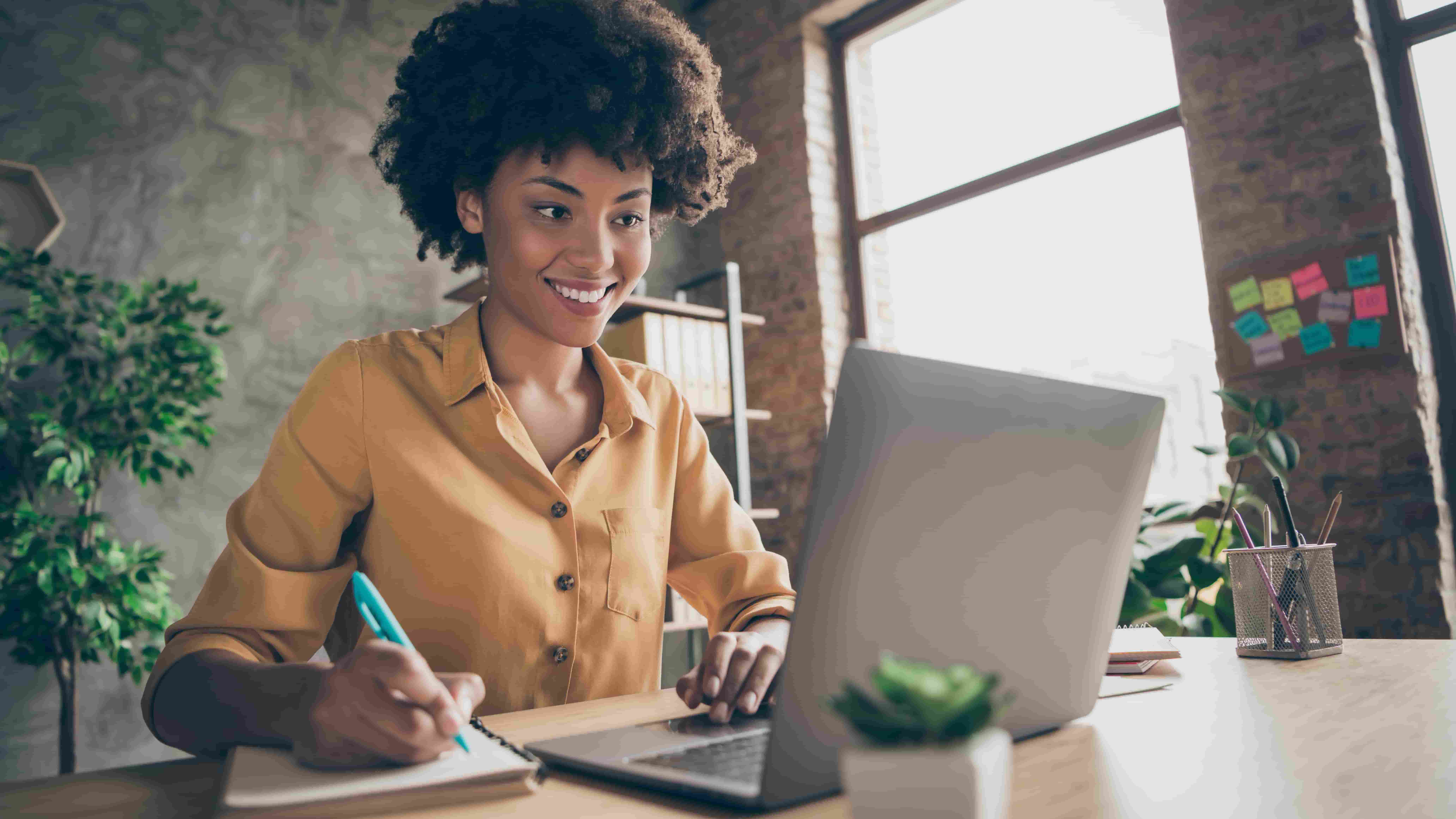 Photo of cheerful joyful mixed-race woman in yellow shirt smiling toothily writing down notes holding training for students to be executives at laptop desktop table